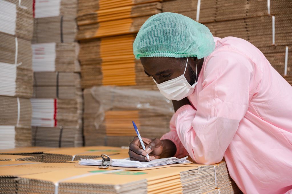 Young African man with headscarf protection and covid-19 safety mask writing on clipboard